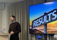 En man står framför en stor skärm som visar en skylt med texten RESULTS