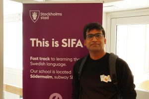 En man står framför en skylt med texten This is SIFA och Stockholms stads logotyp högst upp.