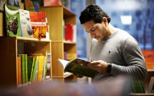 En man läser en bok i ett bibliotek.