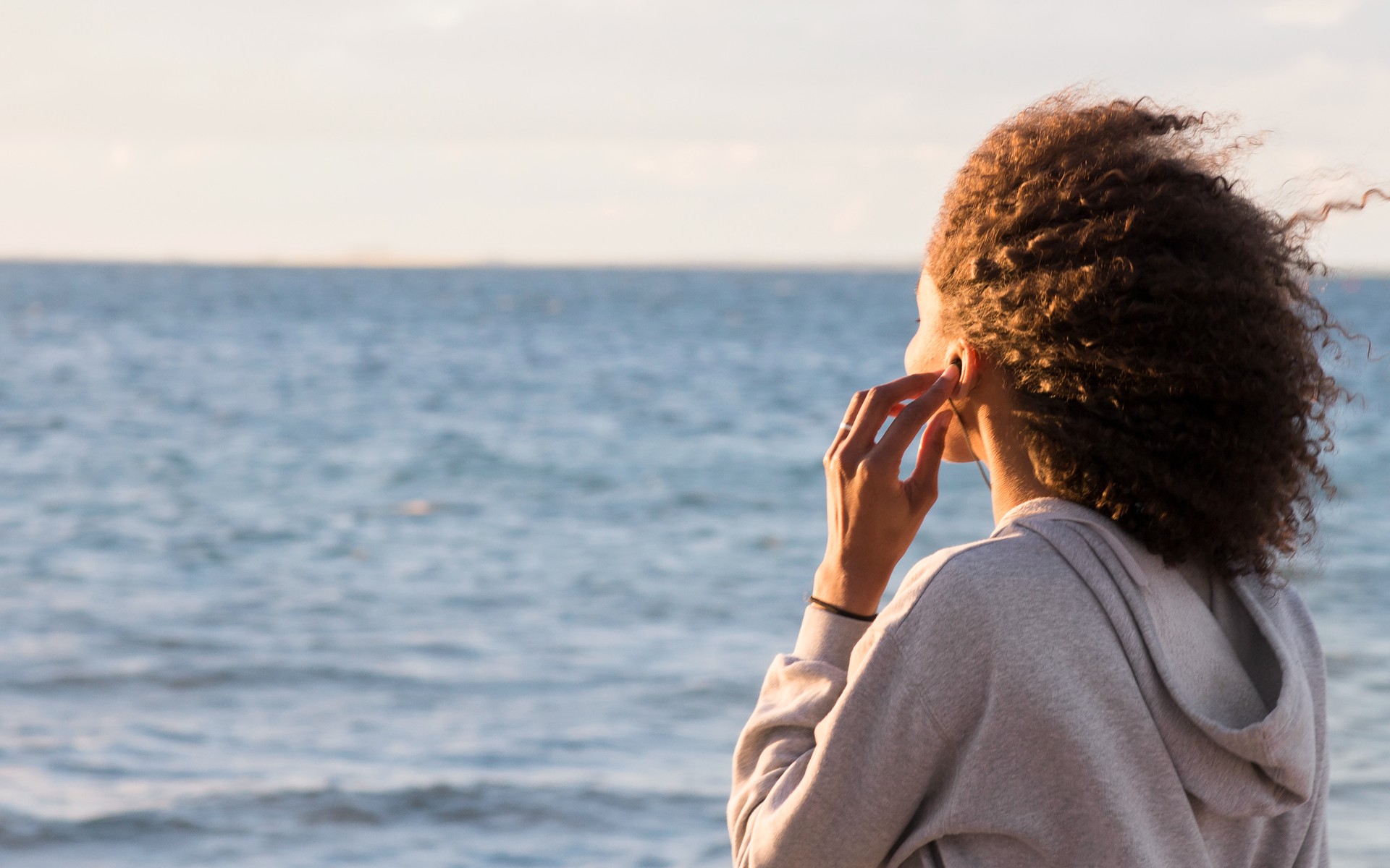 En ung kvinna lyssnar på musik vid havet.