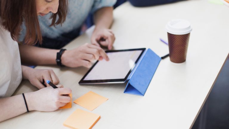 Två vuxelever studerar med iPad och postitlappar.