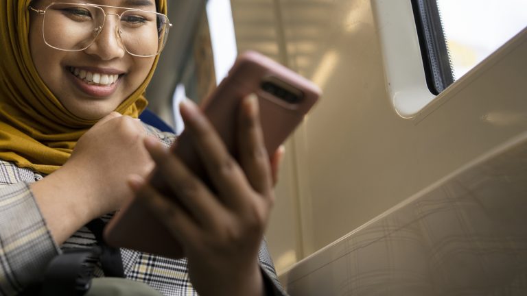 Kvinna med hijab ser på telefonen på tåg.
